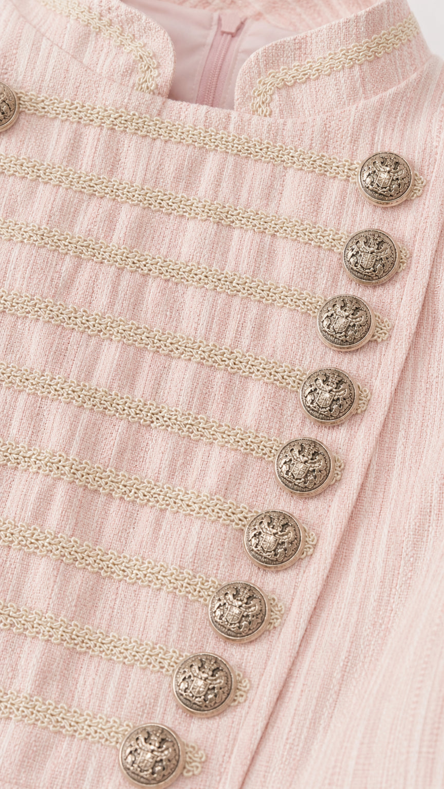 Close-up detail of textured fabric, braided frogging, and embossed crest buttons in blush pink