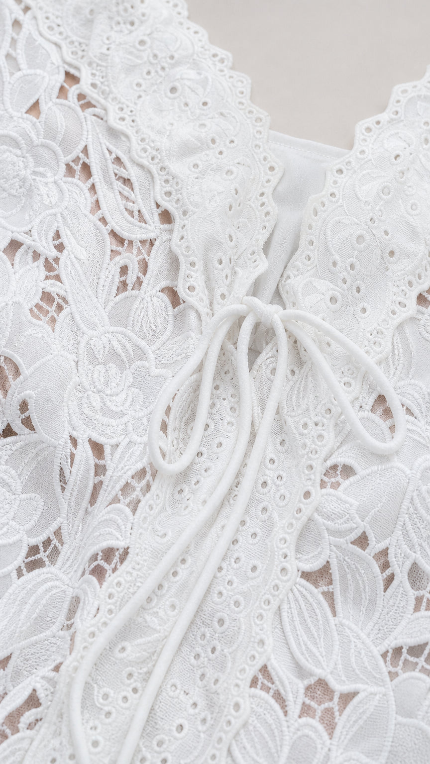 Close-up detail of white floral lace texture, embroidered scalloped neckline, and tie front